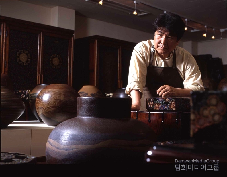  채화칠기 무형문화재 청목 김환경 명인이 자신이 제작한 옻칠공예 작품들 사이에서 작품을 살펴보고 있다. 전통 옻칠기법에 현대적 미감을 더해 ‘회화가 되는 공예, 공예가 되는 회화’를 구현해온 김 명인은 전통공예의 세계화를 위해 꾸준히 창작과 전시활동을 이어가고 있다.
